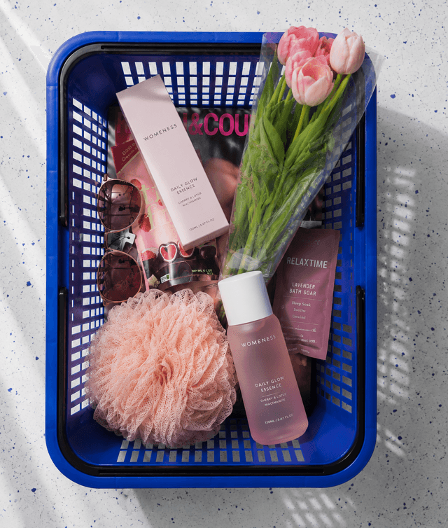 Flatlay of a blue basket packed with pink beauty finds and tulips